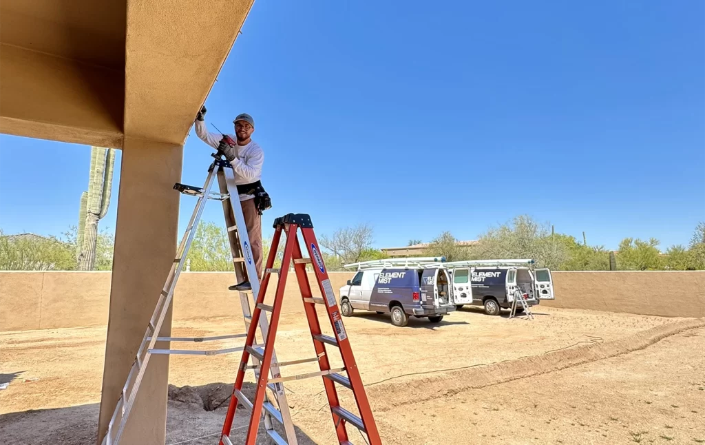 An element mist team member on a ladder installing a misting system in an arizona backyard